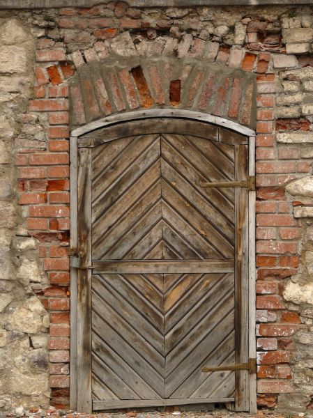 Old wooden door with arching top and diamond pattern on surface.